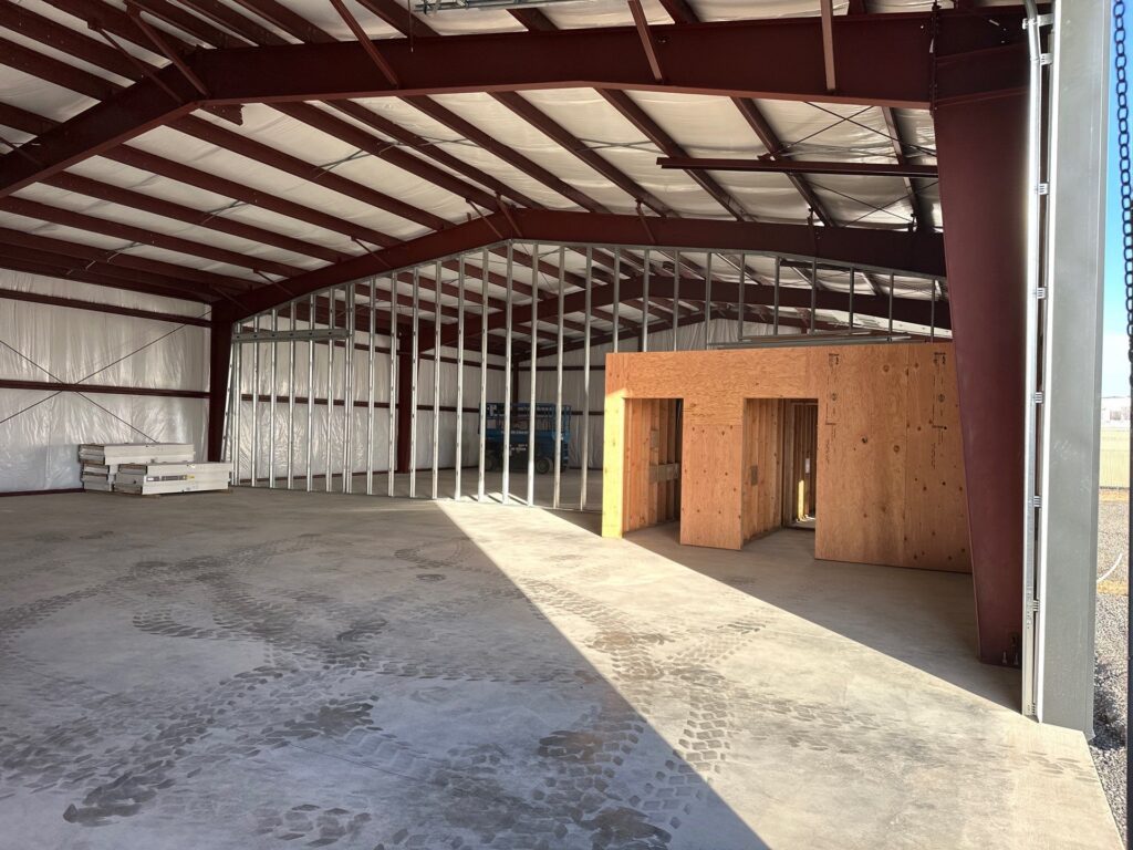 Spacious interior of a pole building with exposed metal framing, open floor space, and high vaulted ceilings.
