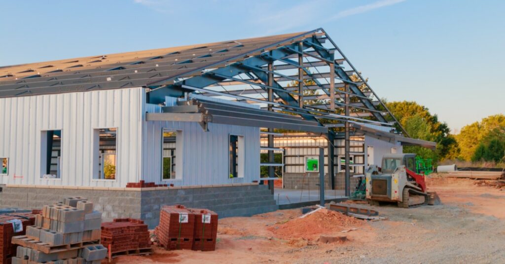 A steel frame and wall panels under construction at a building site with equipment and materials visible.