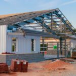 A steel frame and wall panels under construction at a building site with equipment and materials visible.