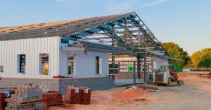 A steel frame and wall panels under construction at a building site with equipment and materials visible.