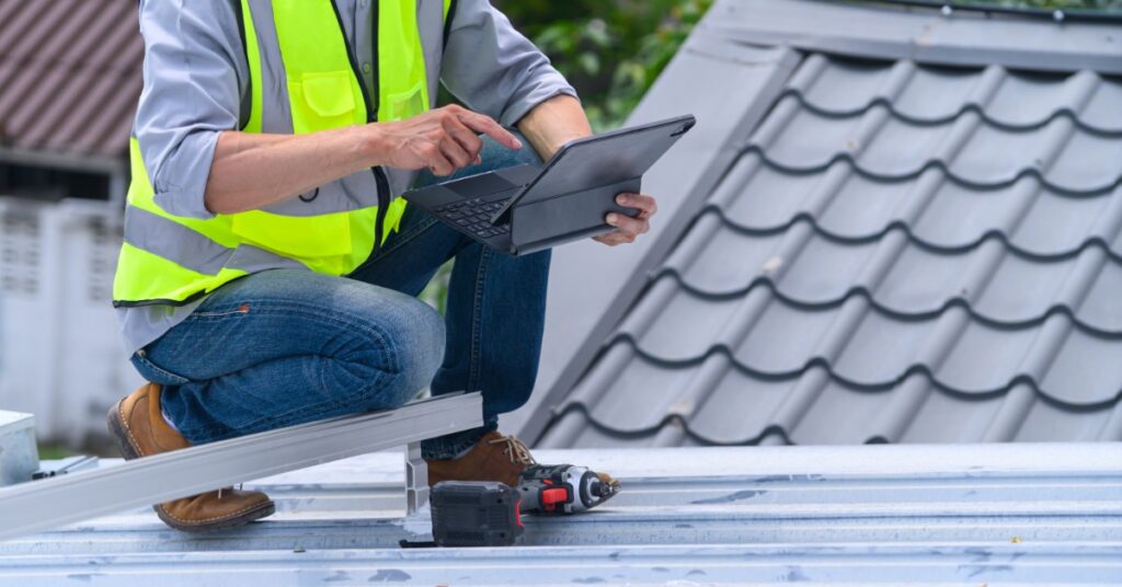A contractor reviews repair details on a tablet while inspecting the metal roof of a commercial building.