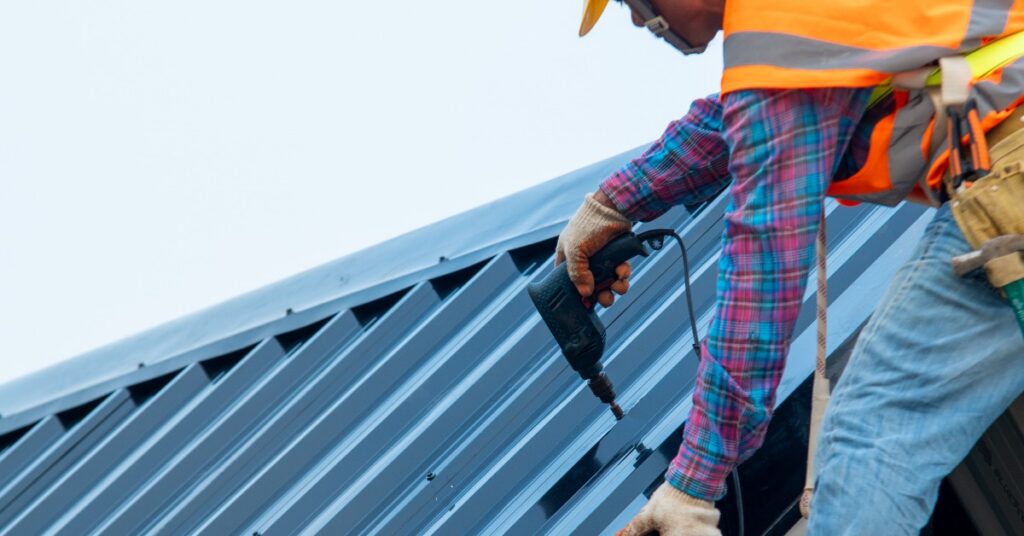 A construction worker uses a drill to secure metal roofing panels during a commercial building repair.