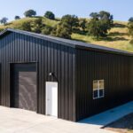 A black metal pole building stands on a rural property with open land surrounding the completed structure.