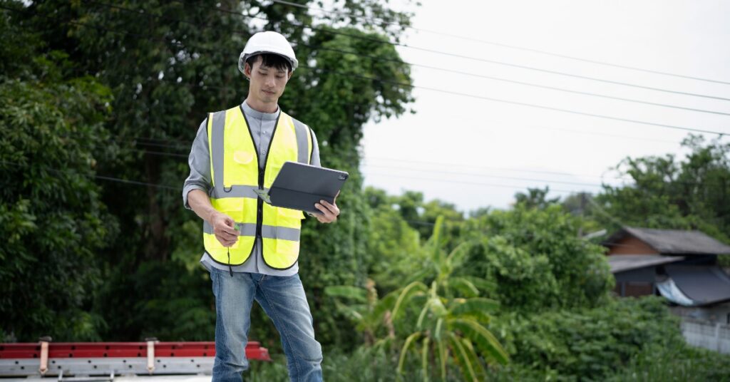 A contractor holding a tablet inspects the metal roof of an existing building before potential expansion work.