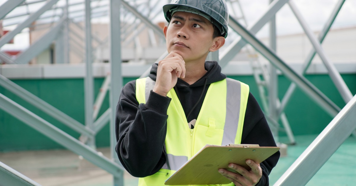 A contractor reviews structural framing with a clipboard while evaluating work at an active construction site.